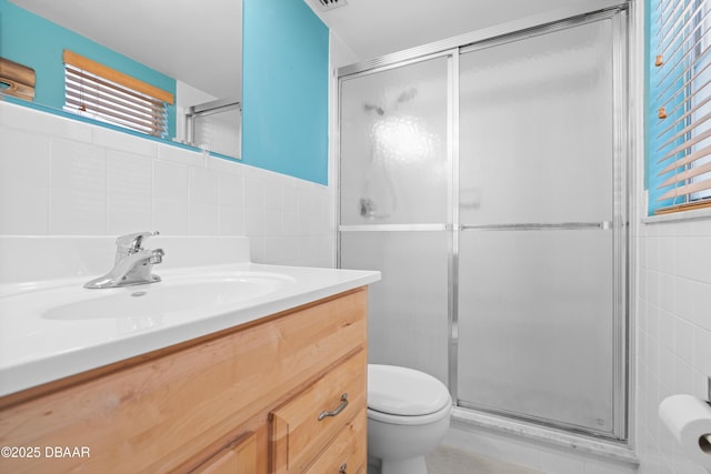 bathroom with tile walls, toilet, a shower with door, and vanity