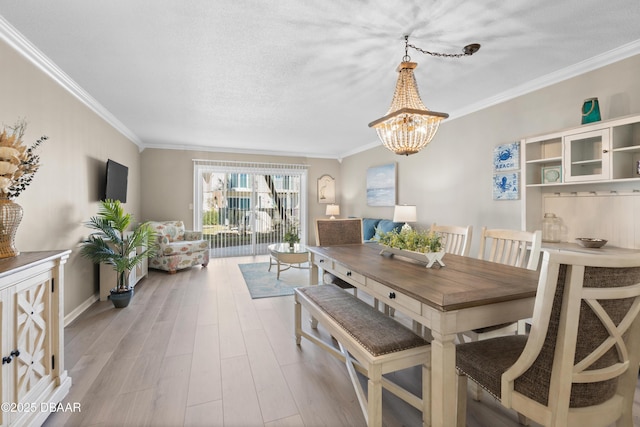 dining space with light wood-type flooring, a textured ceiling, a chandelier, and ornamental molding