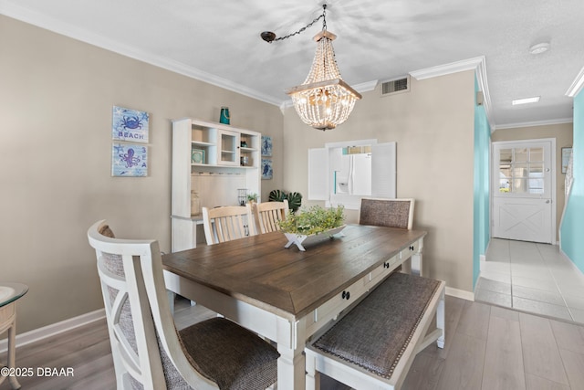 dining space with light wood-type flooring, an inviting chandelier, ornamental molding, and a textured ceiling