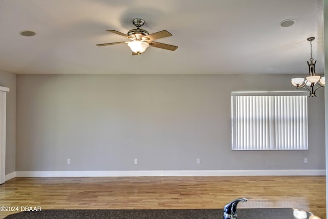 spare room with hardwood / wood-style floors and ceiling fan with notable chandelier