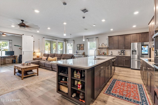 kitchen featuring a kitchen island with sink, sink, stainless steel fridge, a barn door, and dark brown cabinetry