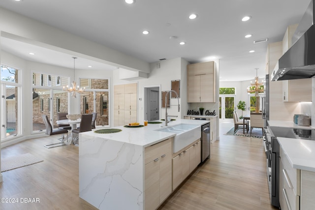 kitchen with hanging light fixtures, a healthy amount of sunlight, wall chimney range hood, and an island with sink