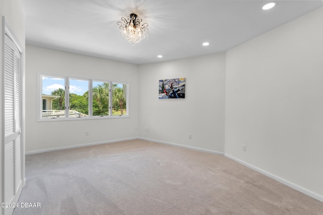 spare room featuring light carpet and a notable chandelier