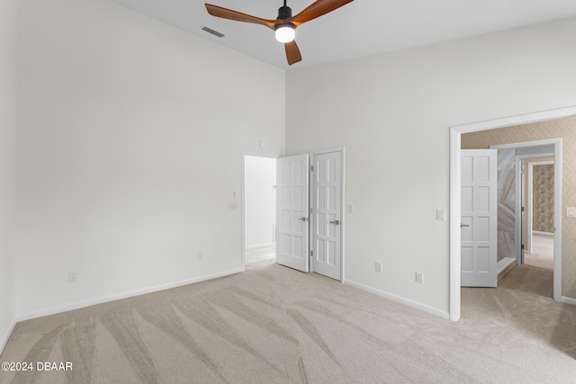 unfurnished bedroom with light colored carpet, ceiling fan, and a towering ceiling