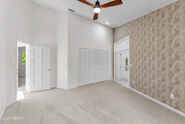 empty room featuring light carpet, a high ceiling, and ceiling fan