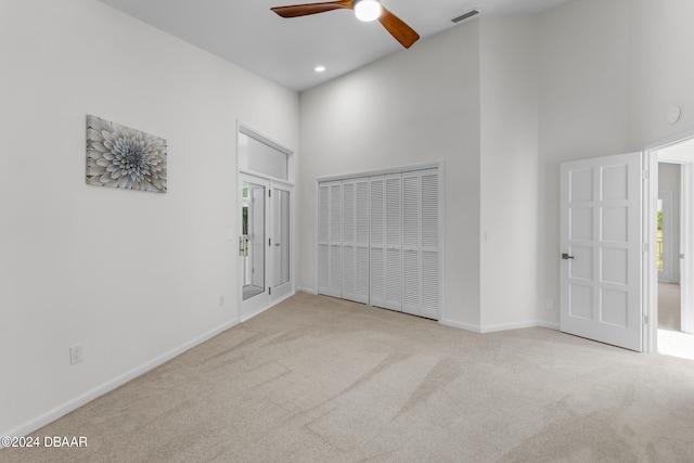 spare room with a towering ceiling, light colored carpet, and ceiling fan