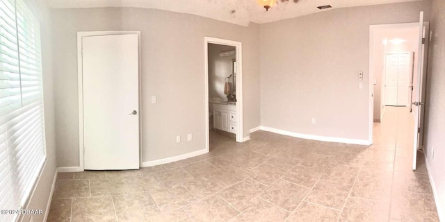 unfurnished bedroom featuring ensuite bath and light tile patterned floors