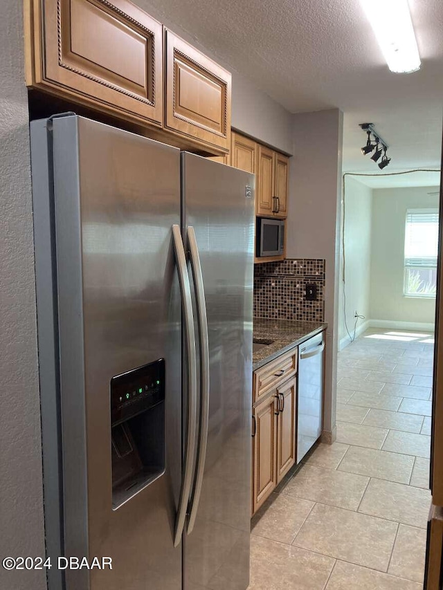 kitchen featuring stainless steel appliances, dark stone counters, a textured ceiling, light tile patterned floors, and decorative backsplash