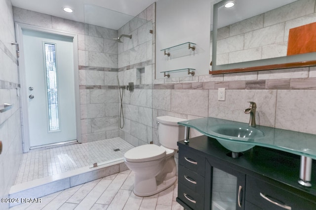 bathroom with vanity, toilet, a tile shower, and tile walls