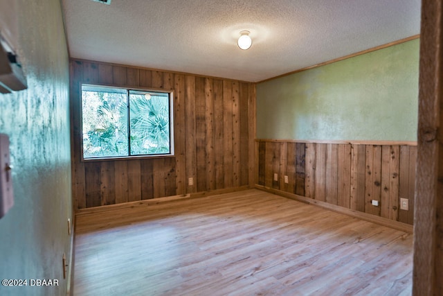 empty room with wooden walls, a textured ceiling, and light hardwood / wood-style floors