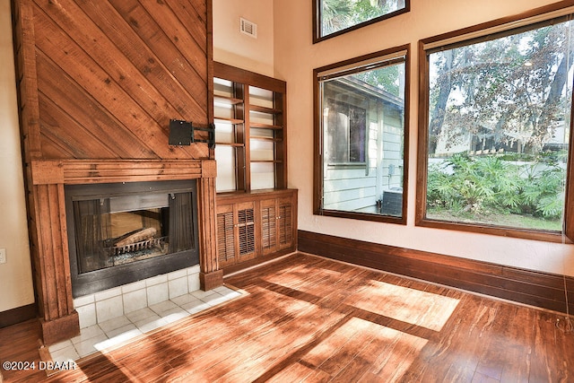 unfurnished living room with a high ceiling, wood walls, a tiled fireplace, and wood-type flooring