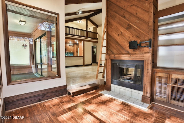 unfurnished living room featuring wood walls, hardwood / wood-style flooring, a tiled fireplace, and vaulted ceiling with beams