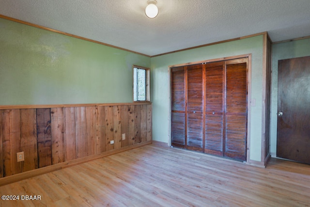 unfurnished bedroom featuring a closet, wooden walls, a textured ceiling, and light hardwood / wood-style flooring