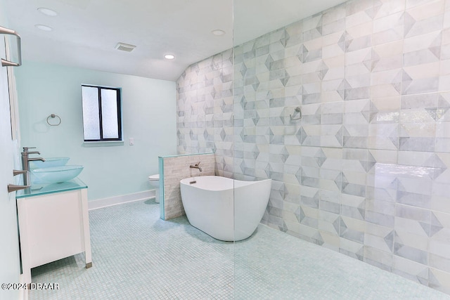 bathroom with tile patterned floors, toilet, tile walls, a washtub, and vanity