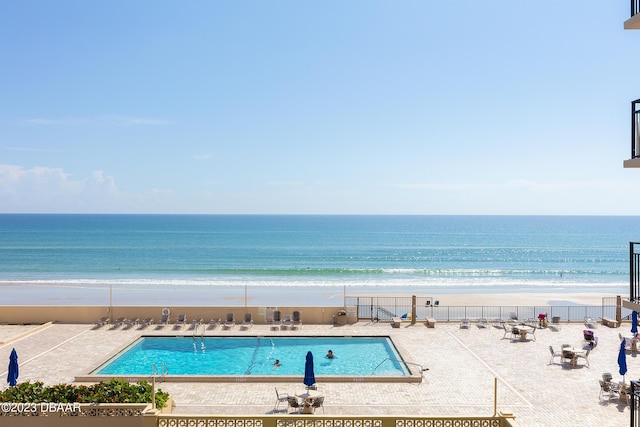 pool featuring a patio, fence, a water view, and a beach view