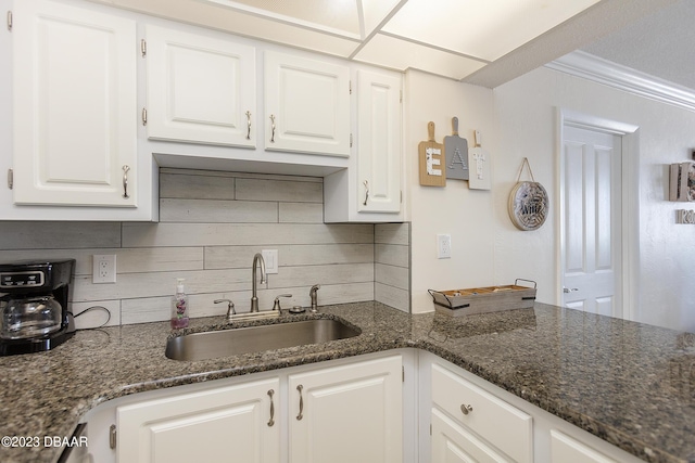 kitchen with a sink, backsplash, dark stone countertops, and white cabinetry