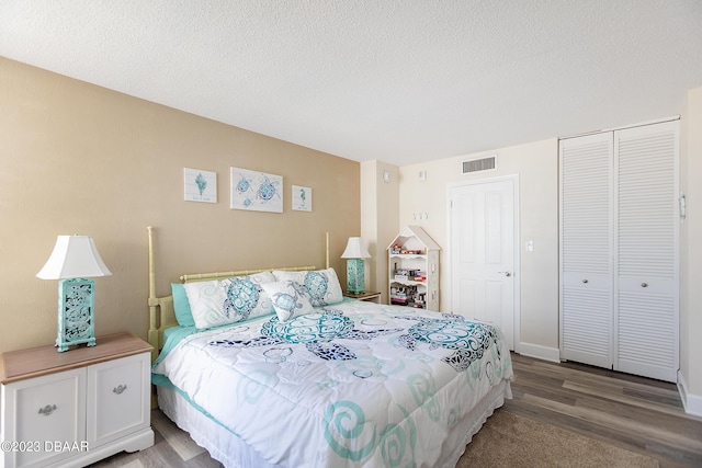 bedroom with visible vents, a textured ceiling, wood finished floors, a closet, and baseboards