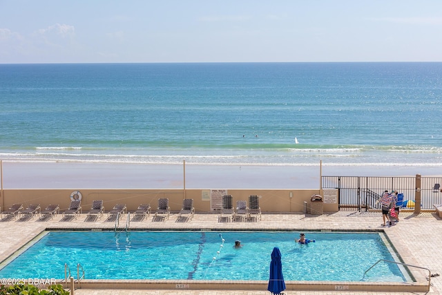 community pool featuring a view of the beach, a water view, and a patio