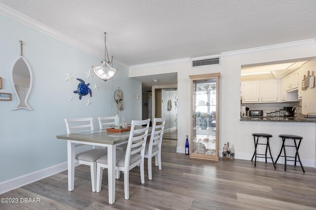 dining area with visible vents, a textured ceiling, crown molding, and wood finished floors