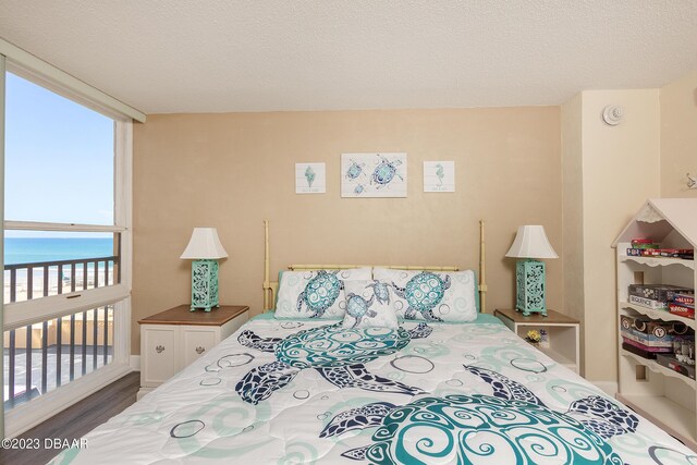 bedroom featuring wood finished floors, a water view, and a textured ceiling