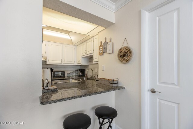 kitchen featuring a toaster, dark stone counters, decorative backsplash, white cabinets, and a sink