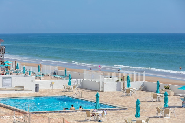 community pool with a beach view, a water view, fence, and a patio area