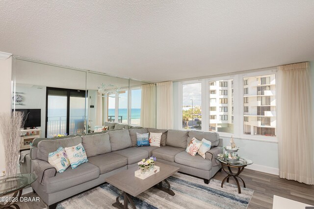 living room with baseboards, a water view, a textured ceiling, and wood finished floors