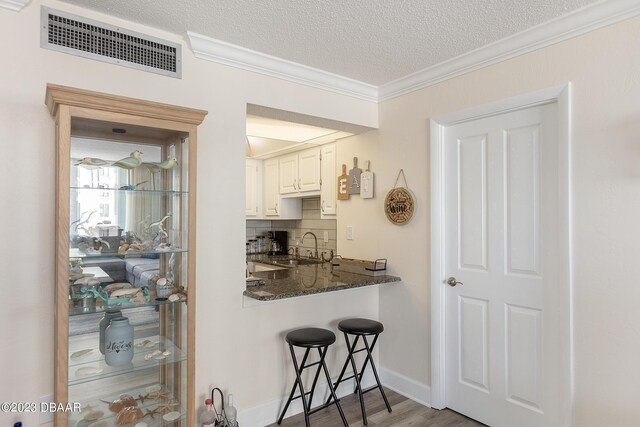 kitchen featuring tasteful backsplash, visible vents, ornamental molding, a textured ceiling, and a sink