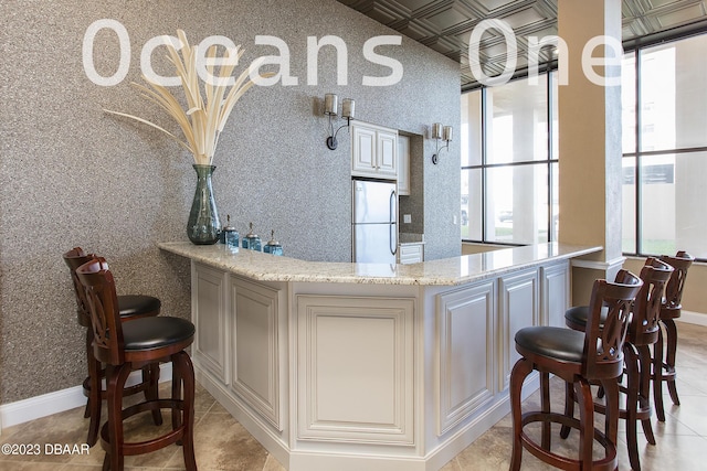 bar featuring light tile patterned floors, baseboards, wallpapered walls, an ornate ceiling, and stainless steel fridge