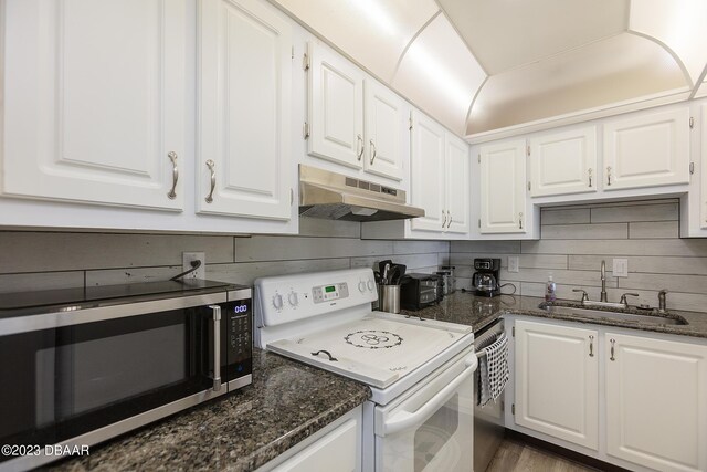 kitchen with dark stone counters, a sink, appliances with stainless steel finishes, under cabinet range hood, and white cabinetry