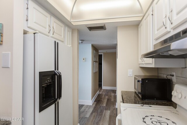 kitchen with visible vents, dark wood-type flooring, white cabinets, white refrigerator with ice dispenser, and under cabinet range hood