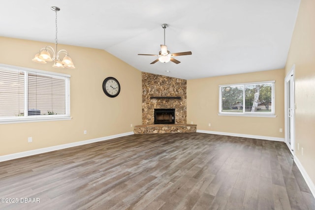 unfurnished living room with hardwood / wood-style flooring, vaulted ceiling, a stone fireplace, and ceiling fan with notable chandelier