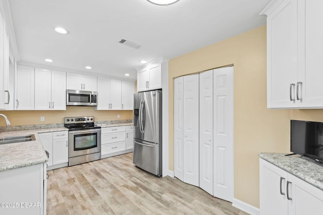 kitchen featuring sink, appliances with stainless steel finishes, light stone countertops, light hardwood / wood-style floors, and white cabinets