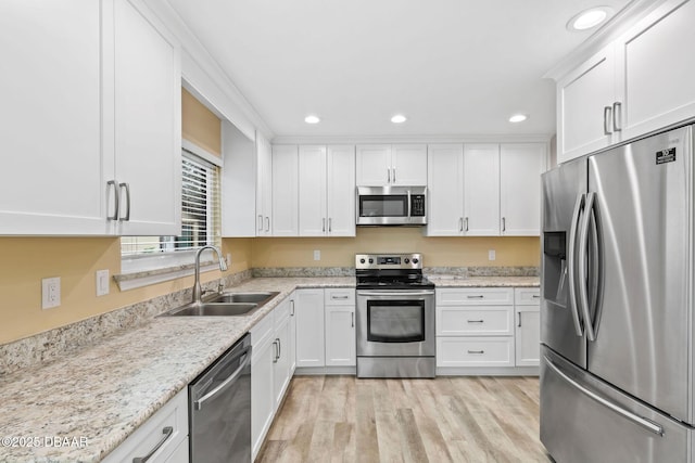 kitchen with sink, stainless steel appliances, light stone counters, white cabinets, and light wood-type flooring