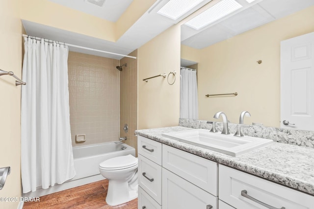 full bathroom featuring a skylight, hardwood / wood-style flooring, vanity, toilet, and shower / bathtub combination with curtain