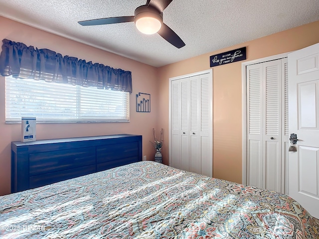 bedroom featuring ceiling fan, a textured ceiling, and multiple closets