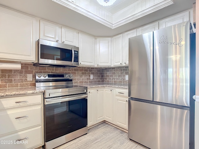 kitchen with ornamental molding, appliances with stainless steel finishes, tasteful backsplash, light stone counters, and white cabinetry