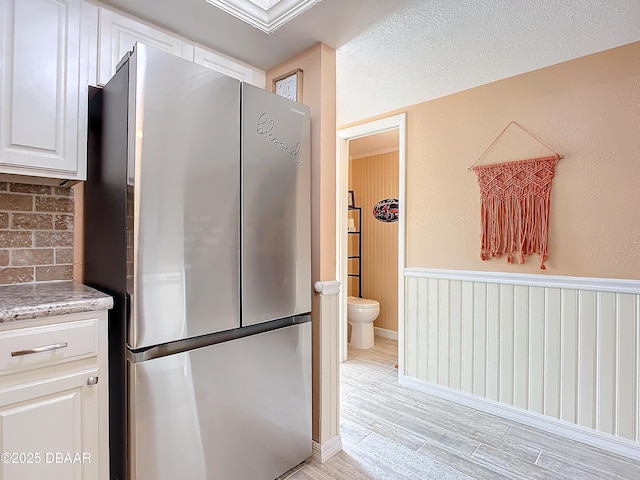 kitchen featuring stainless steel fridge, light wood-type flooring, white cabinetry, and a textured ceiling