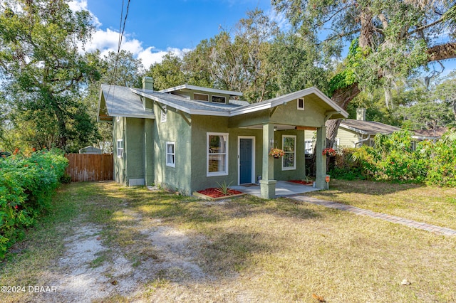 bungalow-style home featuring fence, roof with shingles, stucco siding, a front lawn, and a chimney