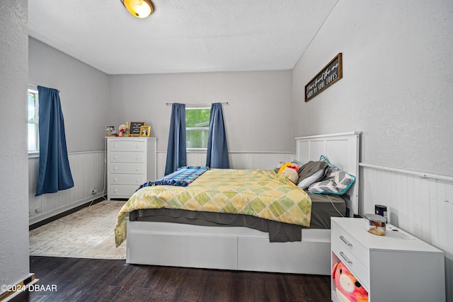 bedroom featuring a wainscoted wall, a textured ceiling, and wood finished floors