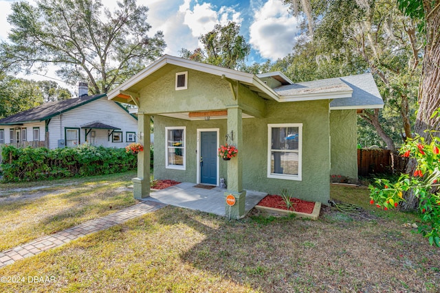 bungalow-style house featuring a shingled roof, a front yard, fence, and stucco siding