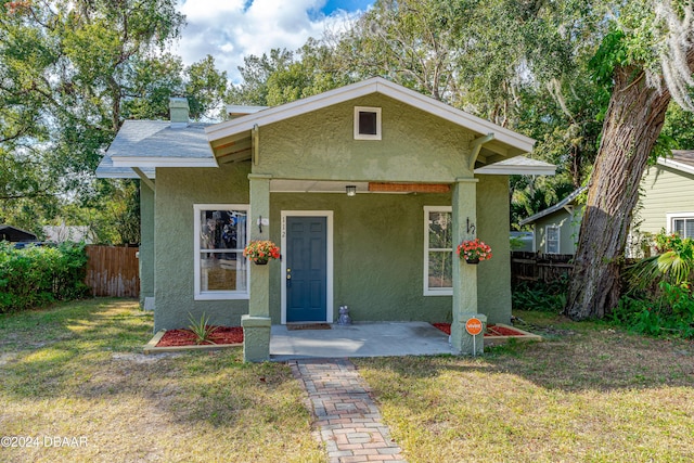 bungalow-style home with roof with shingles, fence, a front lawn, and stucco siding