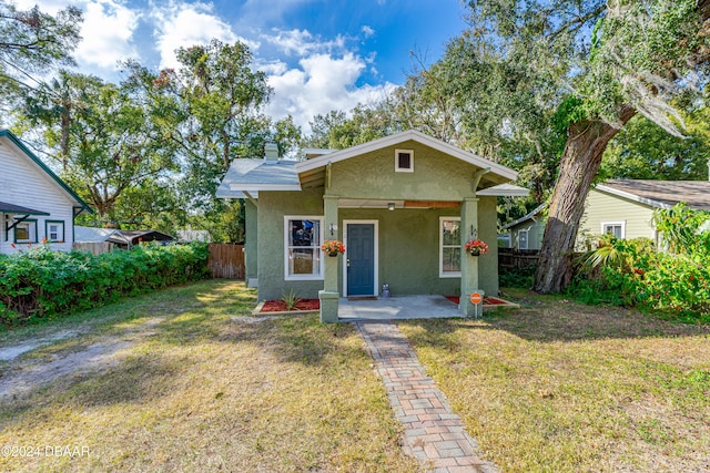 bungalow-style home featuring a front yard, fence, a chimney, and stucco siding