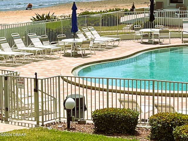 view of swimming pool with a patio, a beach view, and a water view