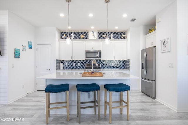 kitchen with stainless steel appliances, white cabinetry, a kitchen island with sink, and pendant lighting