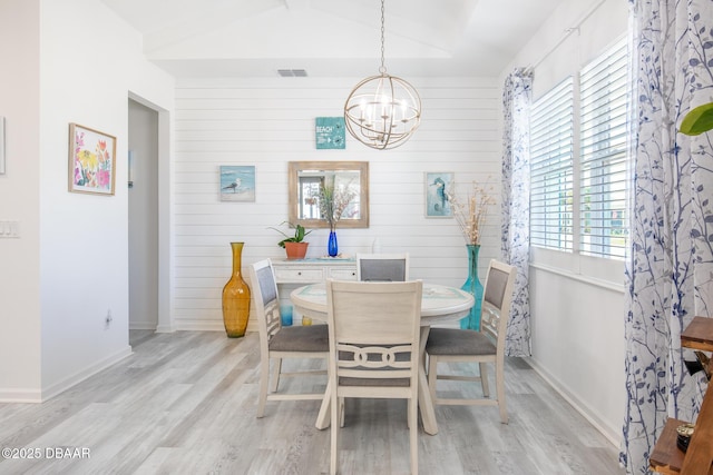 dining area featuring an inviting chandelier, lofted ceiling, wooden walls, and light hardwood / wood-style floors