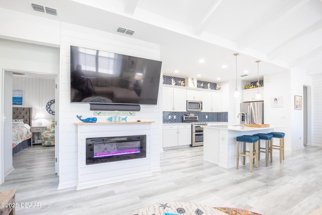 kitchen with appliances with stainless steel finishes, white cabinetry, a kitchen breakfast bar, an island with sink, and decorative light fixtures