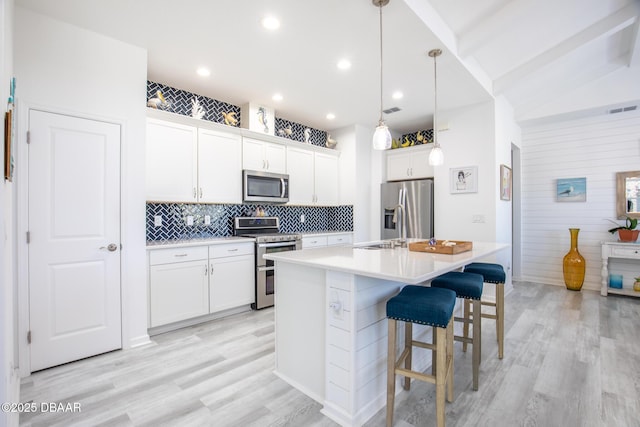 kitchen with appliances with stainless steel finishes, white cabinetry, a kitchen breakfast bar, an island with sink, and decorative light fixtures