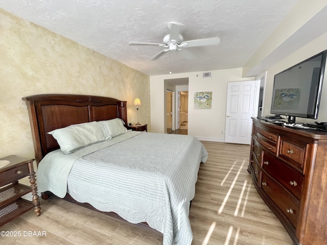 bedroom with ceiling fan, light hardwood / wood-style floors, a textured ceiling, and ensuite bathroom