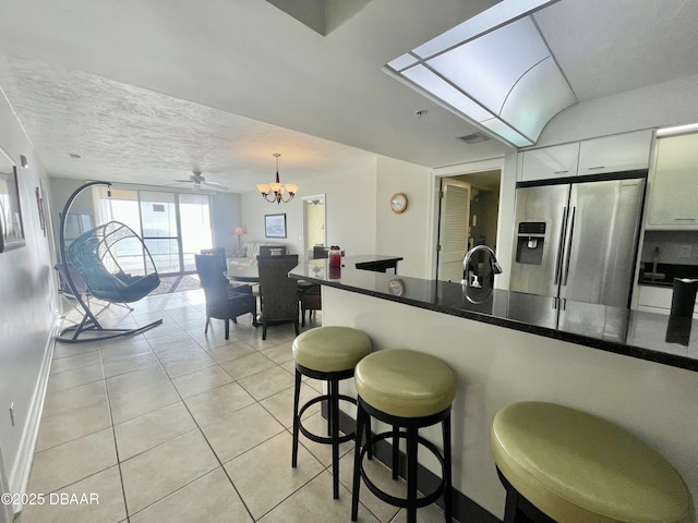 kitchen featuring white cabinetry, light tile patterned floors, stainless steel refrigerator with ice dispenser, decorative light fixtures, and a breakfast bar area